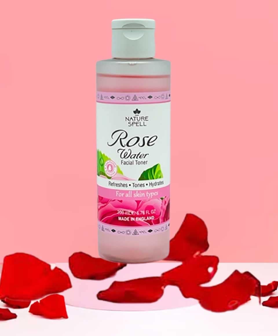 Nature Spell Rose Water Facial Toner from Skin Basics line, in a clear glass bottle with a rose floral label, surrounded by roses.
