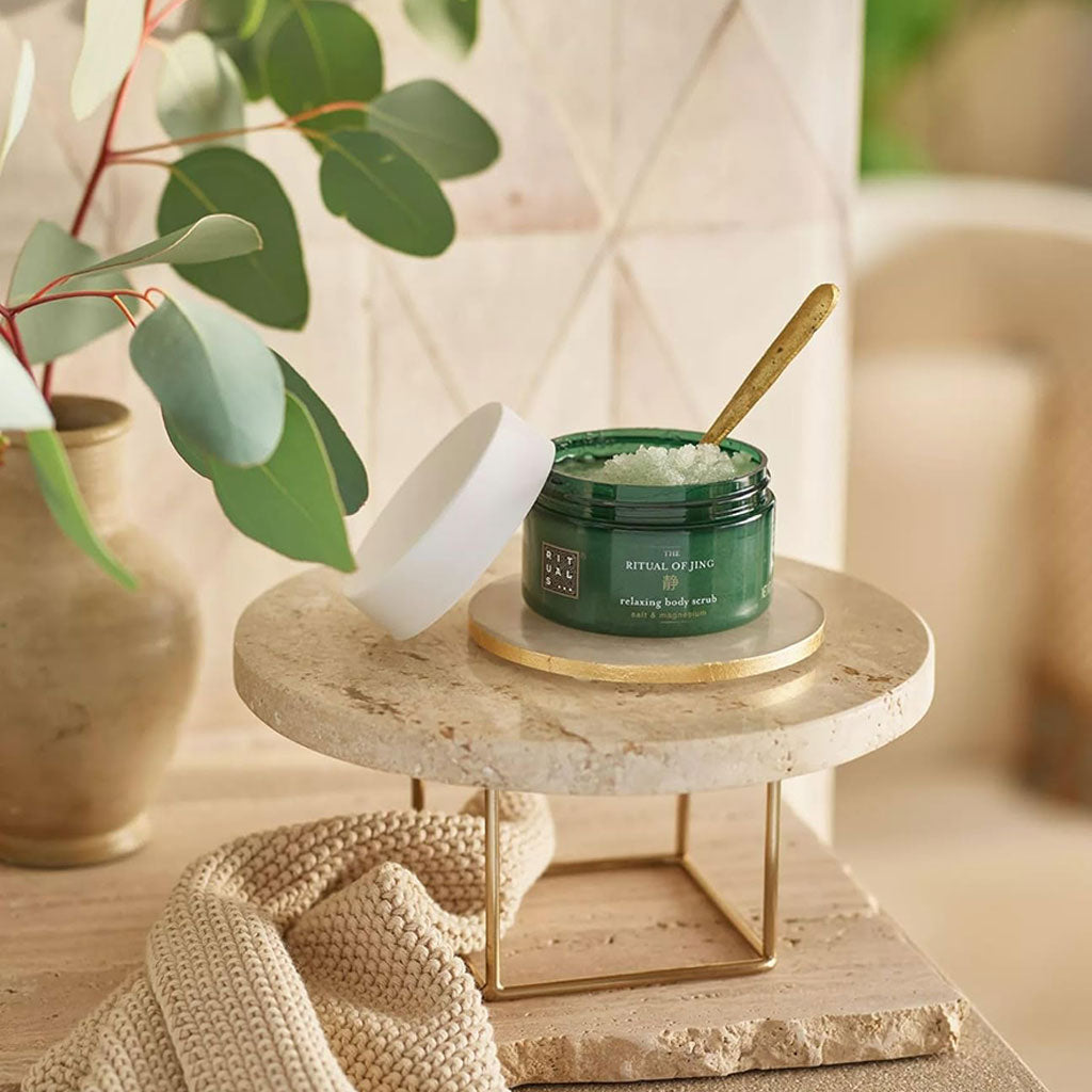 Rituals The Ritual Of Jing relaxing body scrub in a jar, shown with a spoon and natural ingredients, for bath and shower use.